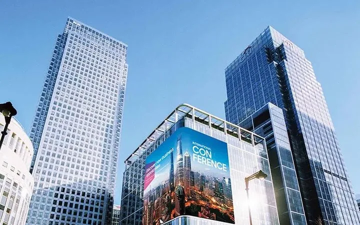 Painel digital de grande formato na fachada de um prédio comercial anunciando um evento, visto da rua