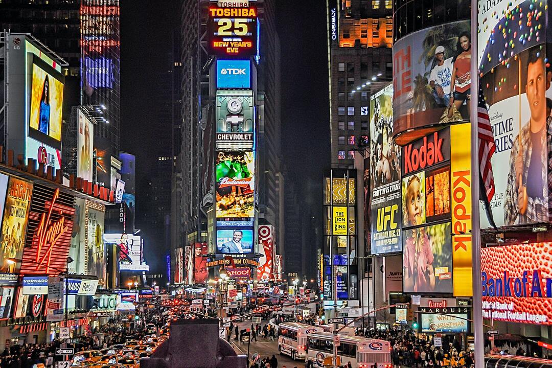 Imagem externa e noturna mostra centro urbano com muitos painéis de led com promoções, campanhas e propagandas ilustrando a sinalização digital