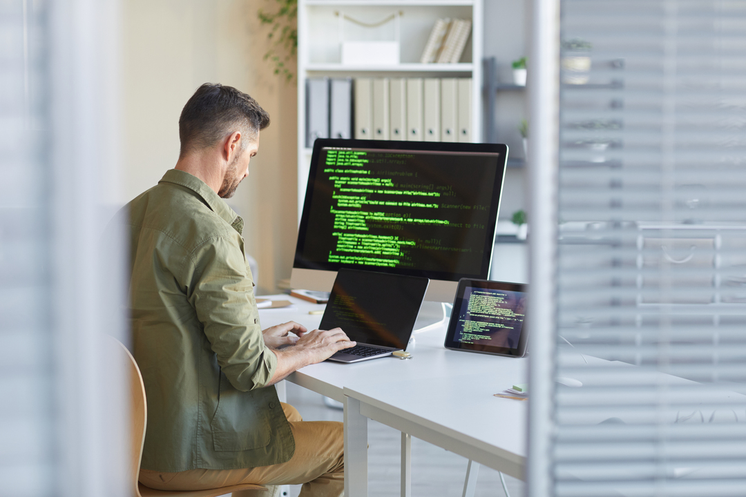Imagem mostra homem mexendo no computador, que está com uma tela em códigos, simbolizando software para digital signage